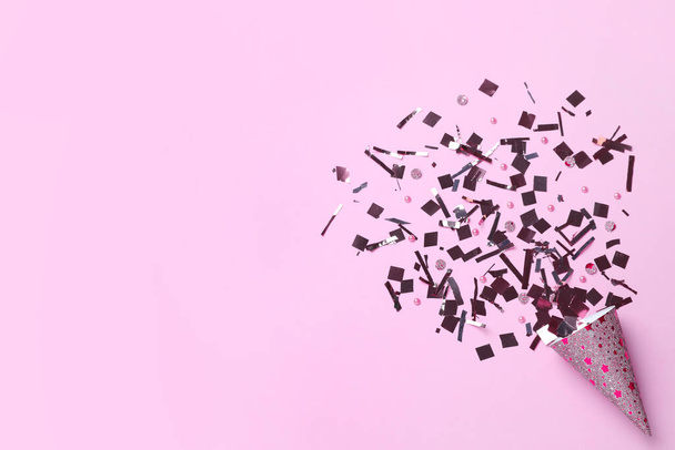 Shiny silver confetti bursting out of party cracker on pink background, top view. Space for text - Foto, afbeelding