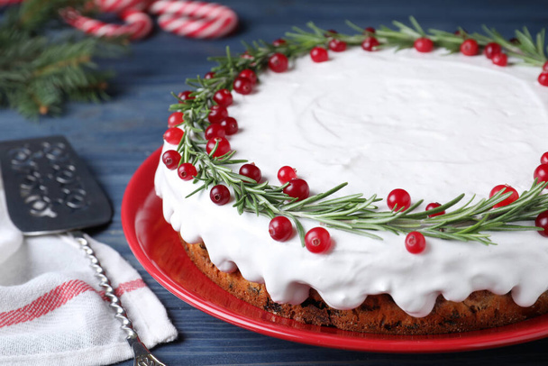 Traditional Christmas cake decorated with rosemary and cranberries on blue wooden table, closeup - Foto, Imagen