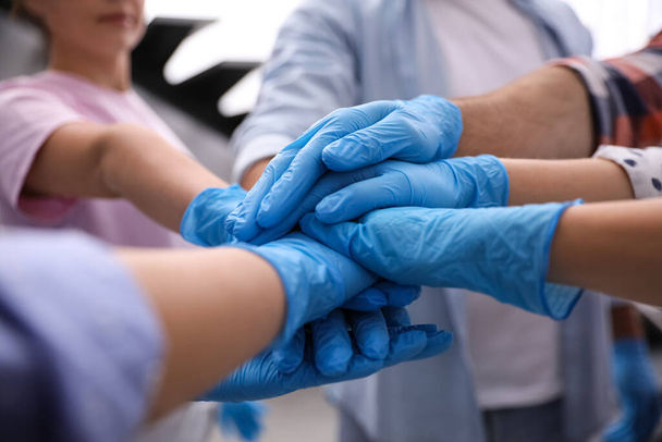 Group of people in blue medical gloves stacking hands indoors, closeup - Foto, Bild