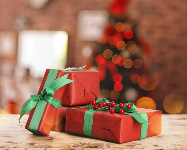 Christmas gift boxes on wooden table in room, bokeh effect - Фото, изображение