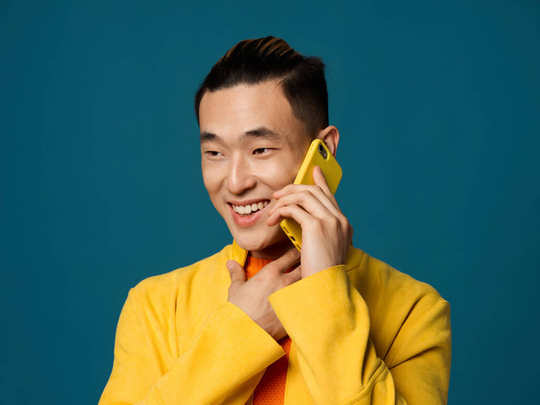 El último asiático está hablando por teléfono sobre un fondo azul y se toca con la mano - Foto, imagen