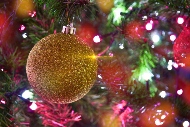 Een gouden bol op kerstgrenen met decoratie van verlichting en bollen. - Foto, afbeelding