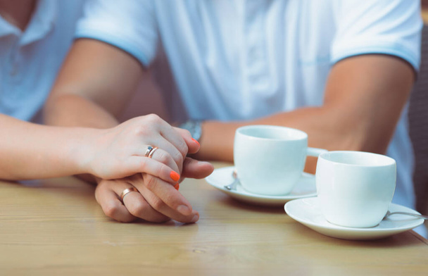 Marry me today and everyday. Close up picture of a couple's hand with golden rings holding each other, wedding picture. Two white coffee cups are on the wooden table. Selective Focu - Foto, Bild