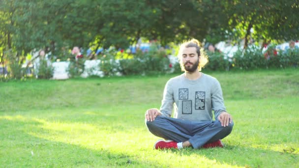 Meditación en condiciones de vida cotidiana. Concepto. Retrato de un joven con ropa casual practicando meditación y relajación en un parque de la ciudad bajo la luz del sol de verano. - Imágenes, Vídeo