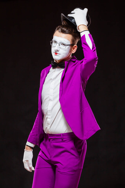 Portrait of male mime artist, isolated on black background. Young man in purple suit is touching his hat in greeting - Foto, Bild