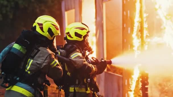 Közelről, két tűzoltó oltja el a tüzet, éjjel locsolják le a házat tömlővel.. - Felvétel, videó
