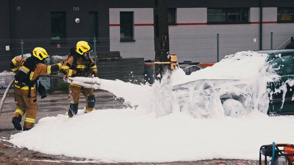 Firefighters extinguish fire from the burning car using foam - Foto, imagen