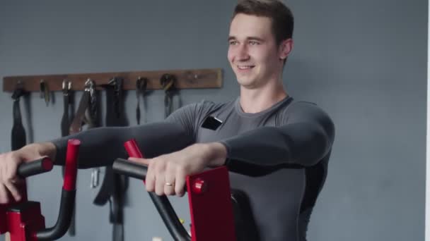 Красивый спортсмен выполняет упражнения на тренажерном аппарате в спортзале - Кадры, видео