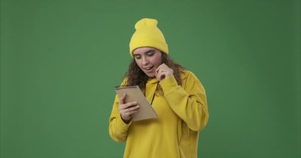 Ecstatic woman writing in notepad over green background - Materiaali, video