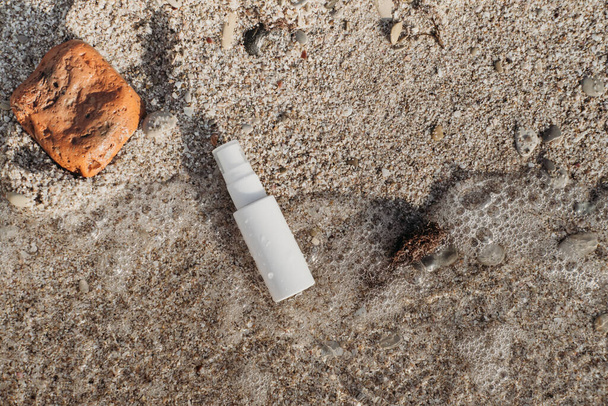 UV-bescherming lotion op een zand gewassen door de zee golf. zonnebrandcrème in ongebrandmerkte witte fles. huidverzorging en antirimpelverzorging. - Foto, afbeelding