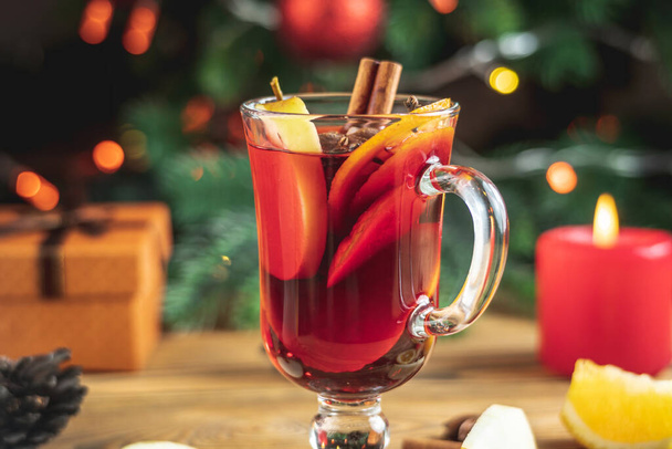 Cup of aromatic hot mulled wine on a wooden table on the background of a Christmas tree with lights. Concept of a festive atmosphere. - Photo, Image