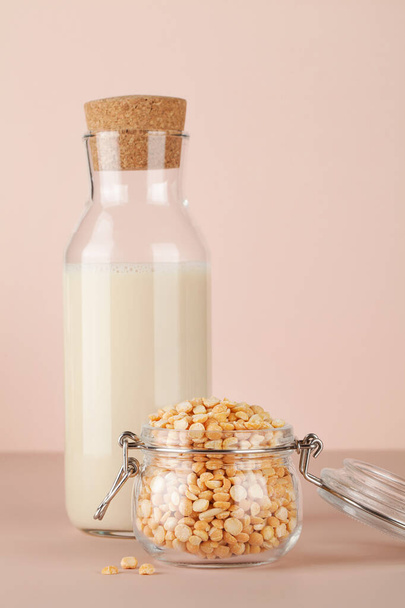 Pflanzliche Erbsenmilch in der Flasche und Erbsen im Glas auf beigem Hintergrund. Glutenfreies, laktosefreies Produkt. Kopierraum. - Foto, Bild