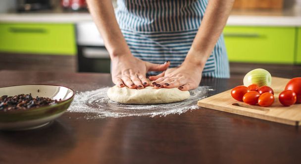 Μια γυναίκα σεφ ζυμώνει ζύμη με τα χέρια της στην κουζίνα για να φτιάξει σπιτική πίτσα.. - Φωτογραφία, εικόνα