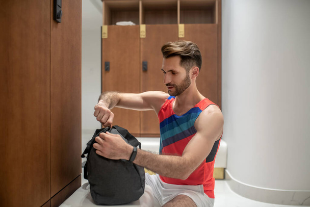 Sporty dark-haired man in bright tshirt unzipping his bag - Valokuva, kuva