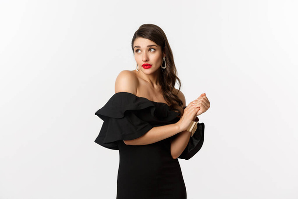Fashion and beauty. Young silly woman in black dress pouting and looking timid, standing in black glamour dress over white background - Photo, Image