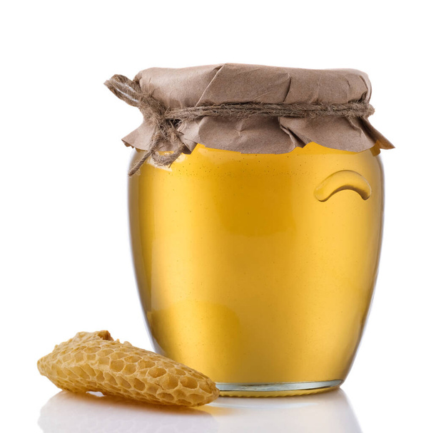 Frasco de vidro cheio de mel e um pedaço de célula de mel um fundo branco - Foto, Imagem