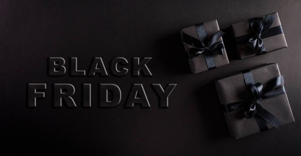 Draufsicht auf schwarze Weihnachtsgeschenkboxen mit schwarzem Band auf schwarzem Hintergrund mit Kopierraum für Text. Zusammensetzung des Black Friday. - Foto, Bild