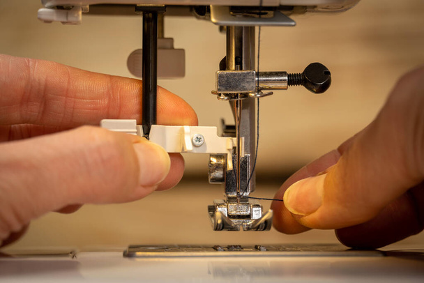 Frauenfingern, die Fäden in Nadelschlaufen auf eine moderne elektrische Nähmaschine legen, um mit dem Nähen zu beginnen. Stahlnadel mit Greifer und Presserfuß. Nahaufnahme von arbeitenden Frauen. Unklarer Hintergrund. - Foto, Bild