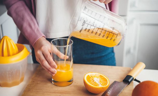 Caucasian woman is putting fresh juice in the glass after squeezing in a manual squeezer - Photo, Image