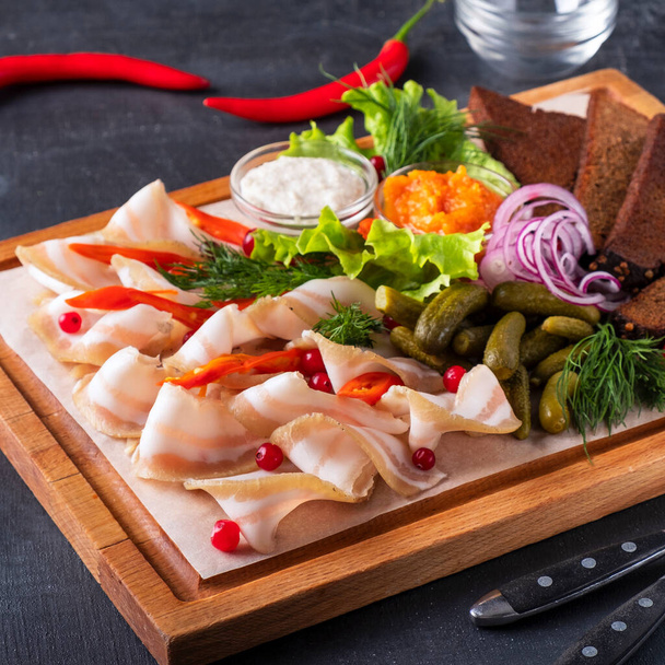 Pork fatback appetizer with crispy bread and pickled cucumbers on a wooden board. Closeup - Foto, Imagem