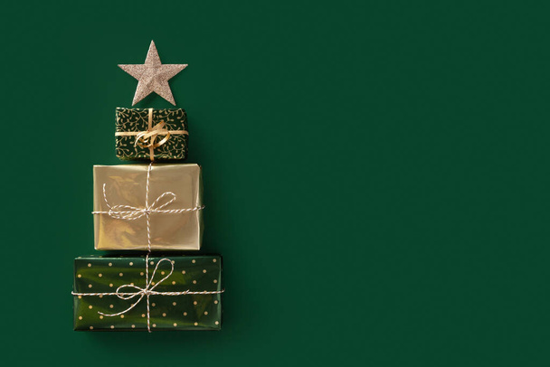 Christmas composition. Three gifts laid out in the shape of a Christmas tree with star on top. Green background. Copy space. - Photo, image
