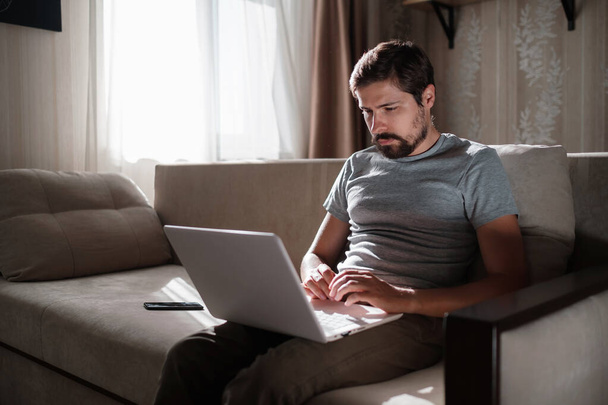 Távoli munka. A férfi, aki laptopon dolgozik, otthon ül a kanapén. Másolja le a helyet a szövegnek. szabadúszó hipster dolgozik otthonról, tanul vagy kommunikál a partnerekkel - Fotó, kép