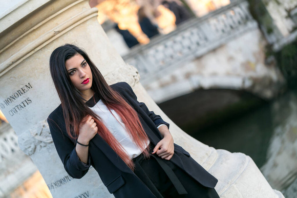 bela morena menina de cabelos longos posando em jaqueta e calças pretas em Pádua. Foto de alta qualidade - Foto, Imagem