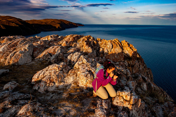Bir kız fotoğrafçı Baykal Gölü yakınlarındaki bir uçurumun kenarında fotoğraf çekiyor. İyi akşamlar. Gökyüzündeki bulutlar. - Fotoğraf, Görsel