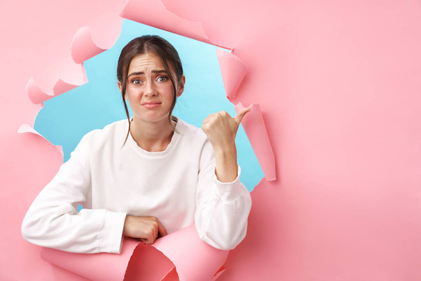 Caucasian young upset woman frowning and gesturing finger at copyspace isolated through pink background - Photo, Image