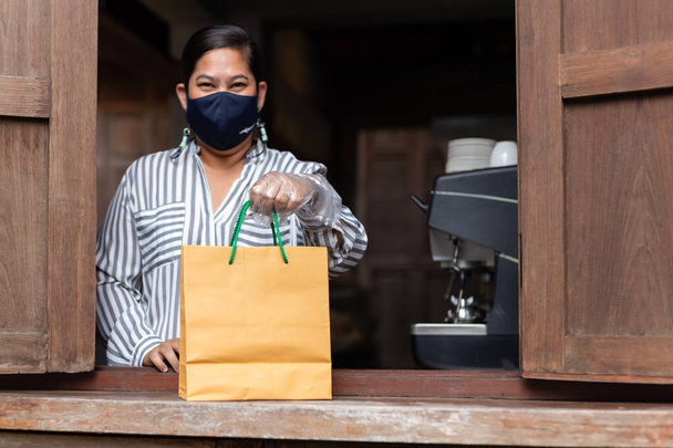 Mulher dono do café com máscara protetora segurando takeaway perto do café janela - Foto, Imagem