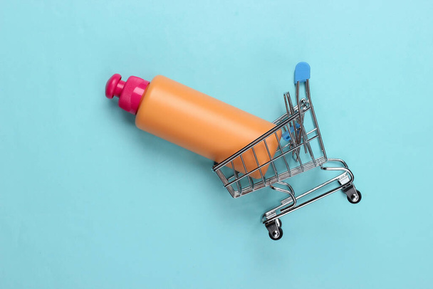 Mini supermarket trolley with shampoo bottle on blue background. Top view - Foto, Imagem