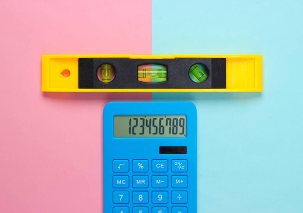 Gebouw niveau en rekenmachine op roze blauwe studio achtergrond. Bovenaanzicht. Minimalisme - Foto, afbeelding