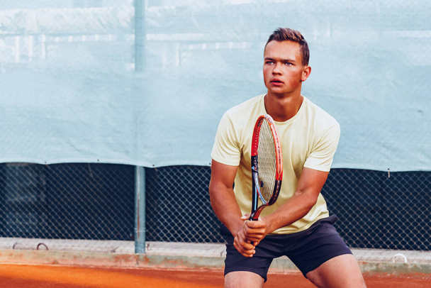 Fiatal jóképű férfi teniszezik a teniszpályán - Fotó, kép