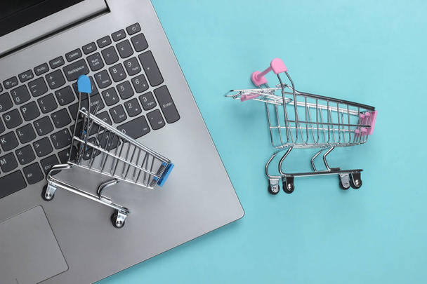 Online-Shopping. Laptop mit Einkaufswagen auf blauem Pastellhintergrund. Ansicht von oben. Flache Lage  - Foto, Bild