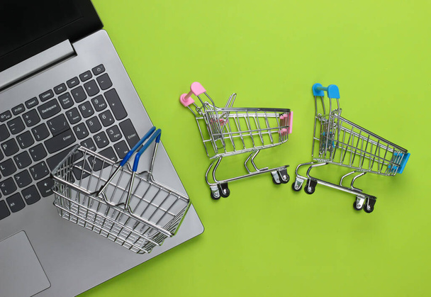 Online nakupování. Laptop se supermarketovými vozíky, košík na zeleném pozadí. Horní pohled. Plocha - Fotografie, Obrázek