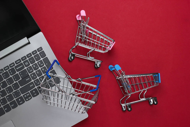 Online nakupování. Laptop se supermarkety vozíky, košík na červeném pozadí. Horní pohled. Plocha - Fotografie, Obrázek