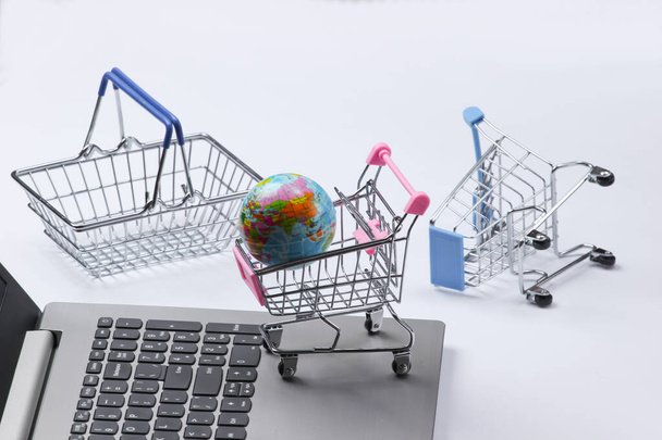 Supermercado global. Compras en línea. Carritos de compras con globo, portátil sobre fondo blanco. Vista superior - Foto, imagen