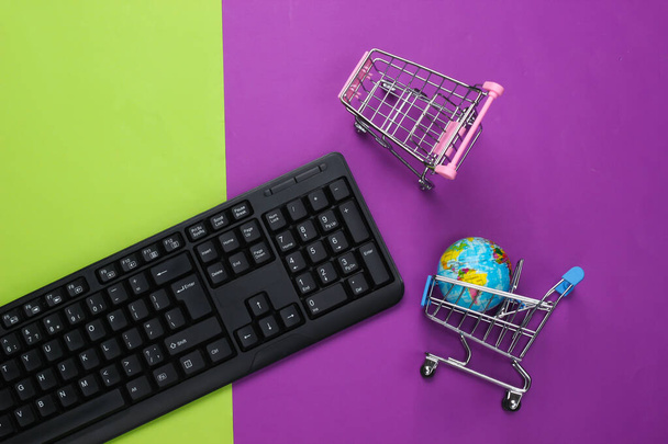 Глобальный супермаркет. Интернет-магазины. Шоппинг тележки с глобусом, клавиатура на фиолетовом зеленом фоне. Вид сверху - Фото, изображение