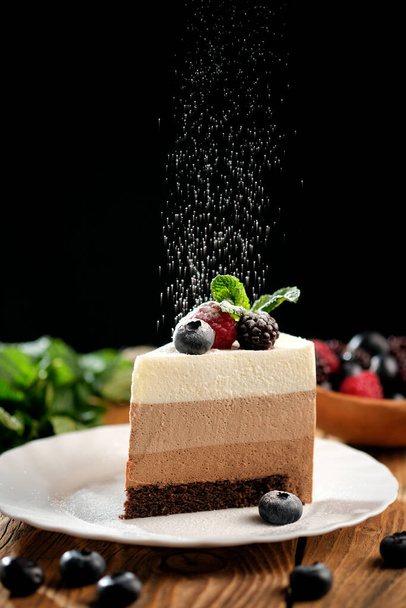 Pedaço de bolo de mousse leve com frutas na superfície de madeira. Receita de bolo de musse para três chocolates - Foto, Imagem