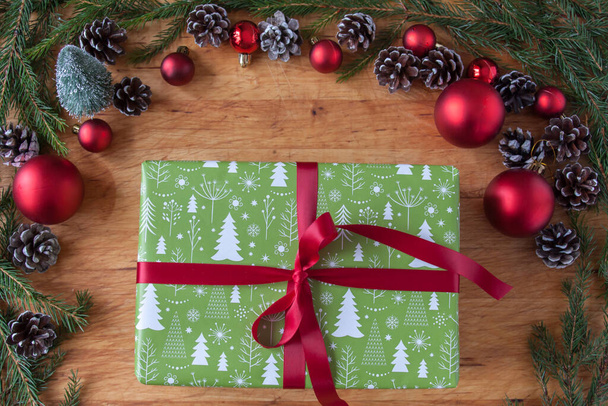 Green christmas gift with red ribbon and ornaments around it - Foto, afbeelding