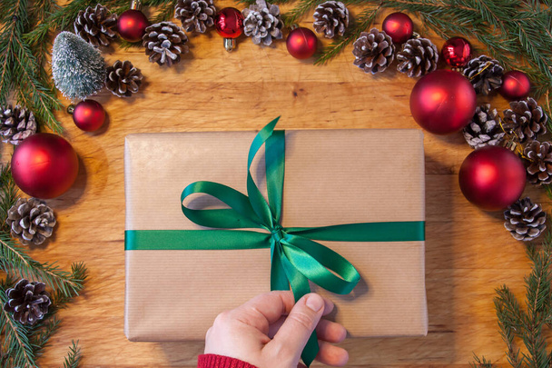 Közelről kéznél próbál kinyitni barna karácsonyi ajándék zöld szalaggal. - Fotó, kép