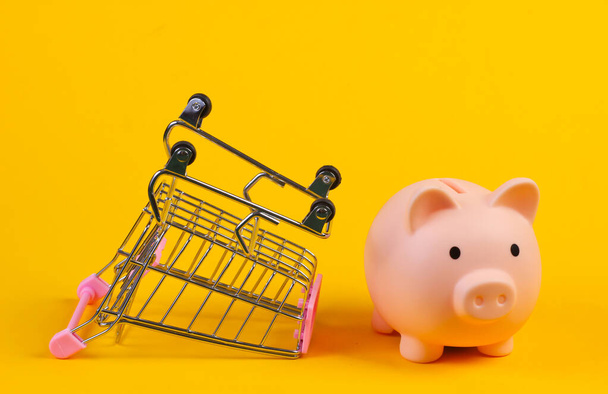 Shopping trolley with piggy bank close-up on yellow background - Fotografie, Obrázek