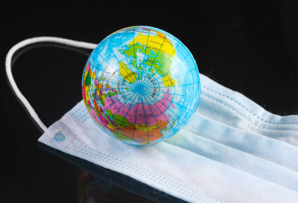 Global pandemic. Medical face mask with globe on black background. Infection prevention and control pandemic covid-19 - 写真・画像