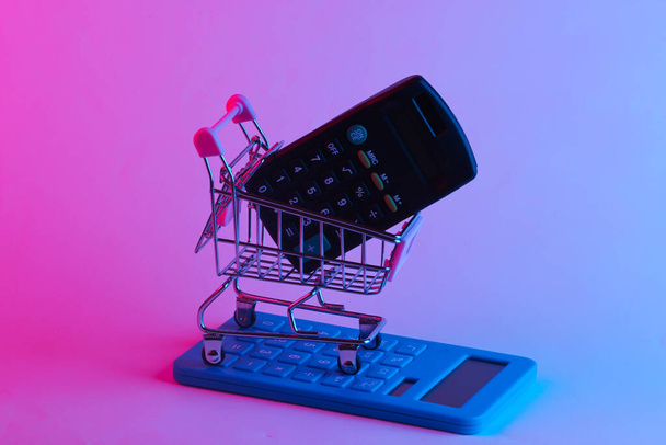 Einkaufswagen mit Taschenrechnern im trendigen Neonlicht. Gradient rosa-blaues Leuchten. Konzeptkunst. Minimalismus - Foto, Bild