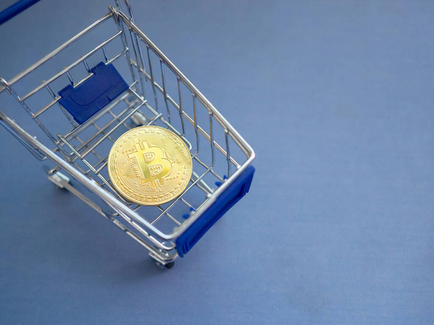 Nahaufnahme eines goldenen Bitcoin im blauen Metallwarenkorb auf blauem Hintergrund mit Kopierplatz für Text. - Foto, Bild