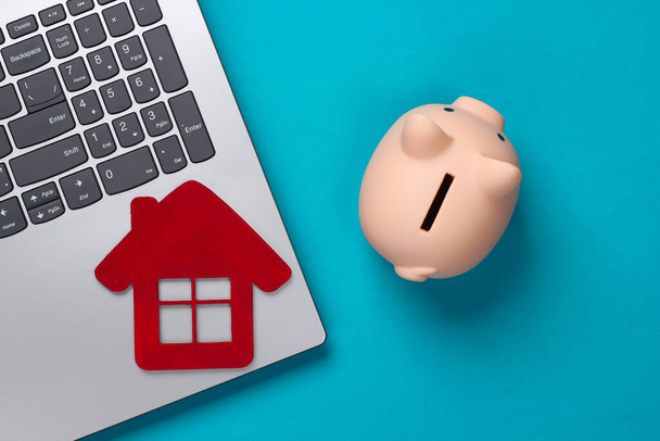 Save up for housing. Laptop, piggy bank with house figure on blue background. Top view - Photo, Image