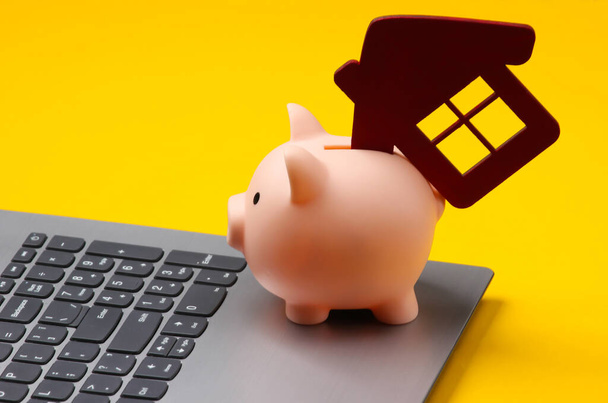Save up for housing. Laptop, piggy bank with house figure on yellow background. - Photo, Image