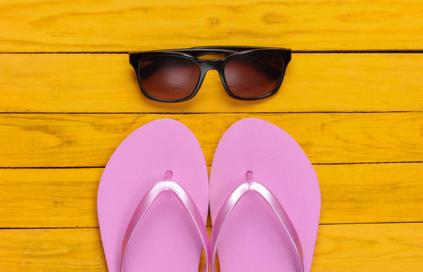 Flip-Flops mit Sonnenbrille auf gelbem Holzgrund. Das Konzept eines Strandurlaubs, eines Resorts. Ansicht von oben - Foto, Bild