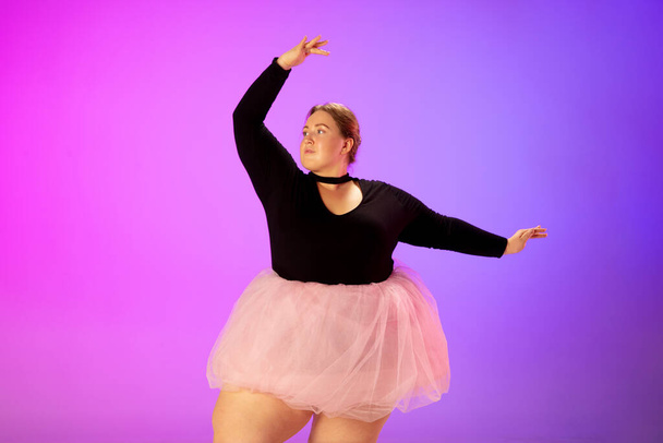 Beautiful caucasian plus size model practicing ballet dance on gradient purple-pink studio background in neon light - Foto, Bild