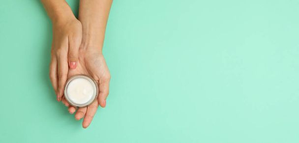Cute female hands hold jar of cosmetic cream on mint background - 写真・画像